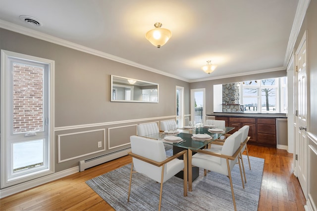 dining space featuring crown molding, light wood-type flooring, and a baseboard heating unit