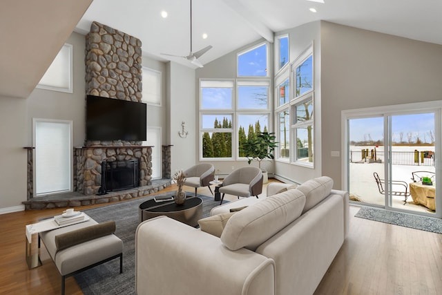 living room with a stone fireplace, light hardwood / wood-style flooring, and high vaulted ceiling