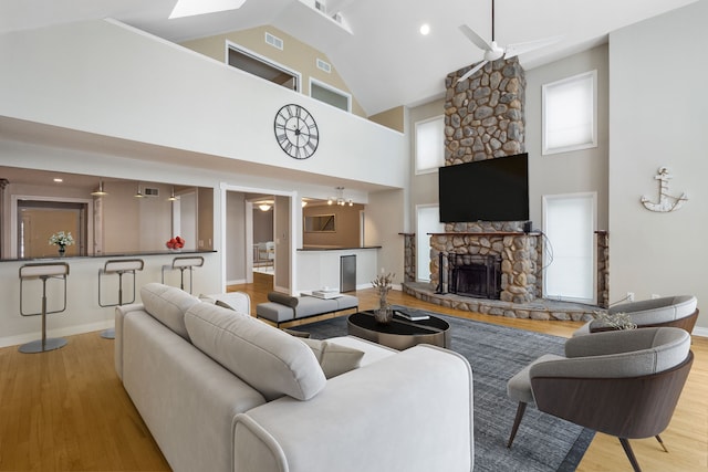 living room featuring ceiling fan, high vaulted ceiling, a fireplace, and light wood-type flooring