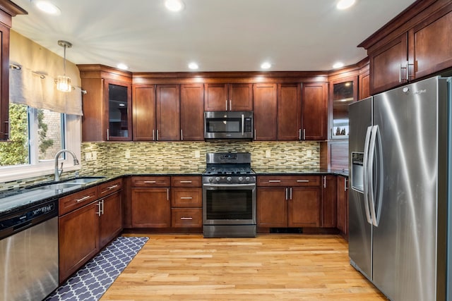 kitchen with sink, dark stone countertops, hanging light fixtures, stainless steel appliances, and light hardwood / wood-style floors