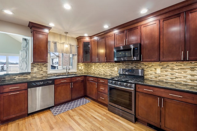 kitchen featuring sink, dark stone counters, hanging light fixtures, stainless steel appliances, and a healthy amount of sunlight