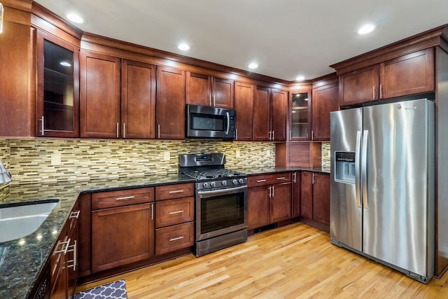 kitchen with sink, dark stone countertops, stainless steel appliances, decorative backsplash, and light wood-type flooring