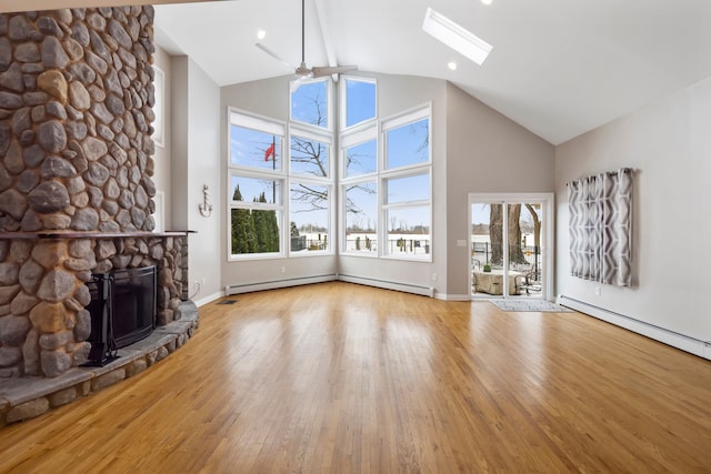 unfurnished living room featuring a baseboard heating unit, a stone fireplace, a skylight, and light wood-type flooring