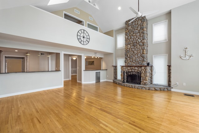 unfurnished living room featuring vaulted ceiling, a stone fireplace, ceiling fan, and light hardwood / wood-style flooring