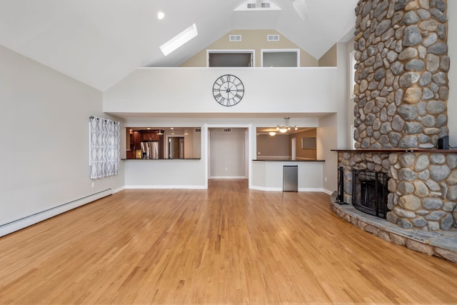 unfurnished living room with baseboard heating, a stone fireplace, a skylight, and light hardwood / wood-style floors