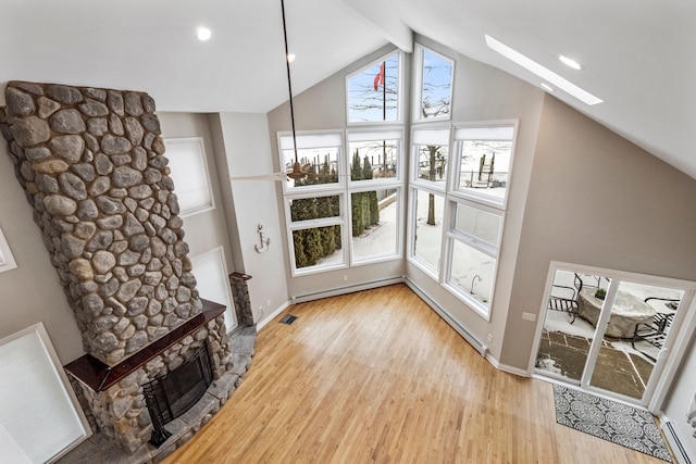 living room with a stone fireplace, lofted ceiling with skylight, and light wood-type flooring