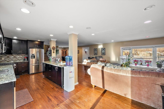 kitchen featuring ornate columns, appliances with stainless steel finishes, wood-type flooring, decorative backsplash, and light stone counters