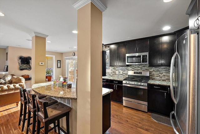 kitchen featuring ornate columns, dark hardwood / wood-style floors, a kitchen breakfast bar, stainless steel appliances, and decorative backsplash