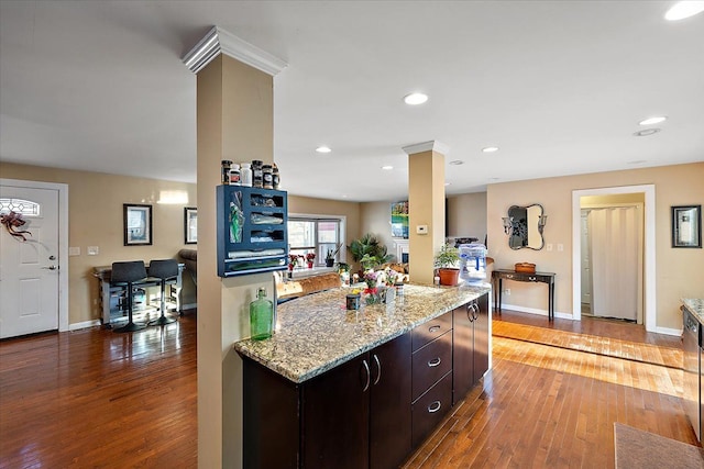 kitchen with ornate columns, light stone counters, dark brown cabinetry, and light hardwood / wood-style floors