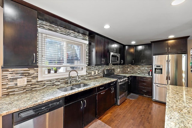 kitchen with stainless steel appliances, light stone countertops, sink, and dark brown cabinets