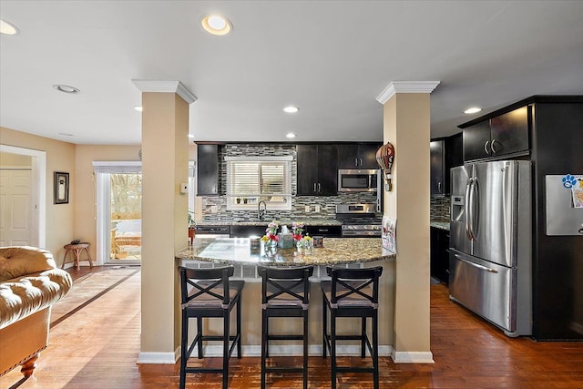 kitchen featuring appliances with stainless steel finishes, dark hardwood / wood-style floors, decorative columns, backsplash, and light stone countertops