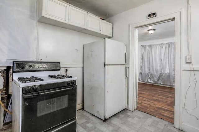 kitchen with white cabinetry, gas stove, and white fridge