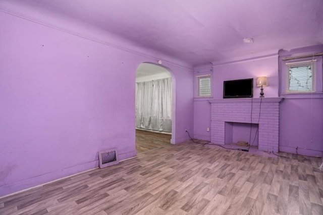 unfurnished living room featuring a wealth of natural light, a brick fireplace, and light wood-type flooring