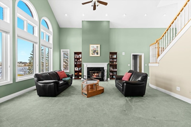 carpeted living room with ceiling fan, a fireplace, and a high ceiling