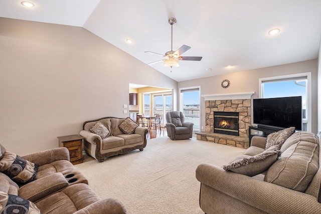 living room featuring vaulted ceiling, carpet, a stone fireplace, and ceiling fan