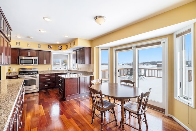 kitchen featuring a kitchen island, appliances with stainless steel finishes, sink, dark hardwood / wood-style flooring, and light stone countertops