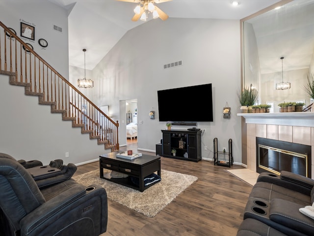 living room featuring ceiling fan with notable chandelier, high vaulted ceiling, hardwood / wood-style floors, and a tile fireplace