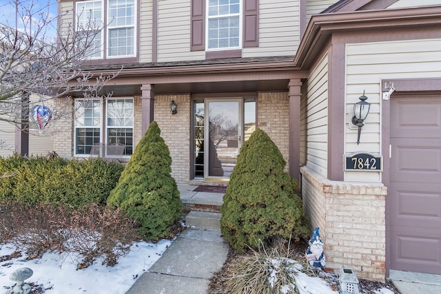 snow covered property entrance with a garage and a porch