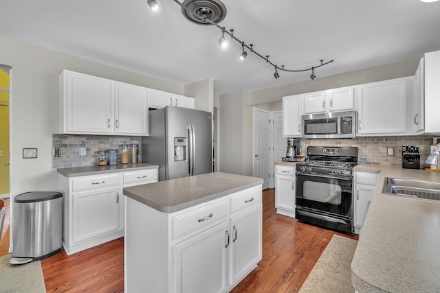 kitchen with hardwood / wood-style flooring, appliances with stainless steel finishes, white cabinetry, a center island, and decorative backsplash