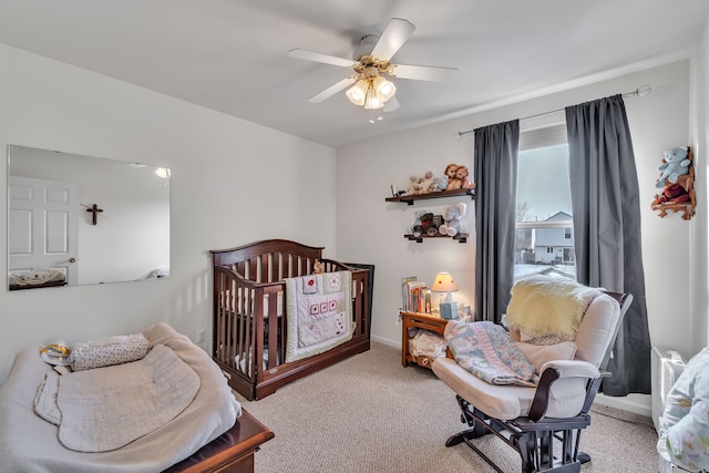 carpeted bedroom featuring a nursery area and ceiling fan