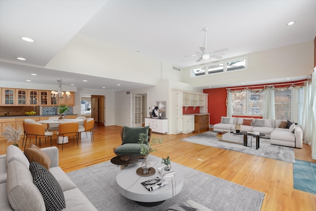 living room featuring ceiling fan with notable chandelier, light hardwood / wood-style flooring, and a high ceiling