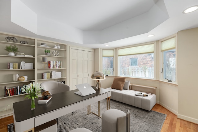 office space with built in shelves, a tray ceiling, and light hardwood / wood-style flooring