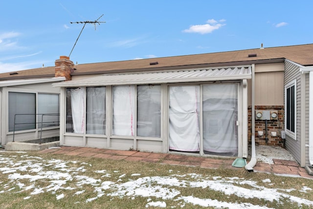 snow covered back of property with a sunroom