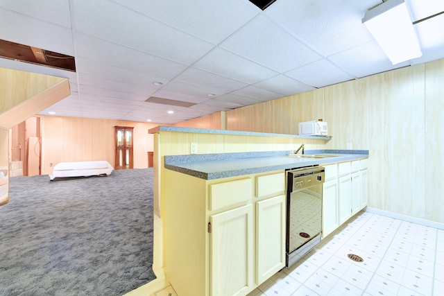 kitchen featuring dishwasher, sink, a paneled ceiling, and wood walls