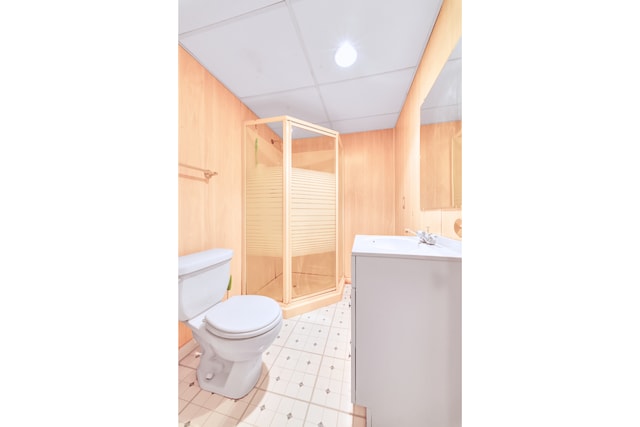 bathroom featuring a paneled ceiling, vanity, an enclosed shower, toilet, and wood walls