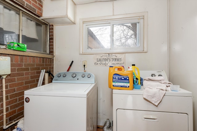 clothes washing area featuring washer and clothes dryer and brick wall