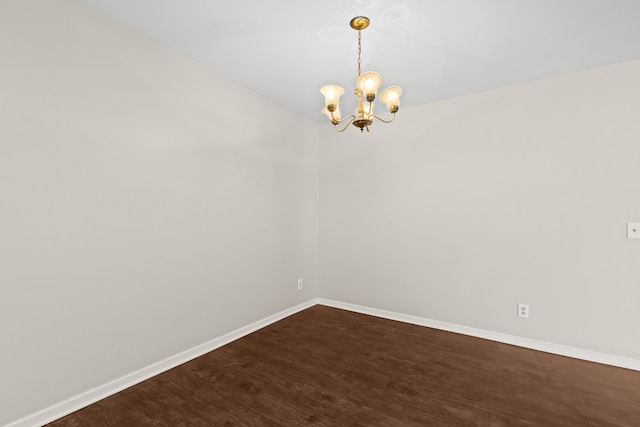 spare room featuring an inviting chandelier and dark hardwood / wood-style floors