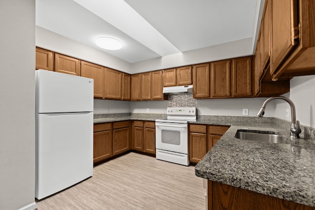 kitchen featuring sink, dark stone counters, white appliances, and light hardwood / wood-style floors