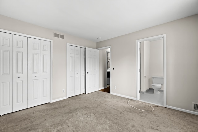 unfurnished bedroom featuring connected bathroom, dark carpet, and multiple closets