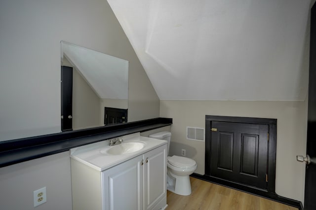 bathroom featuring hardwood / wood-style flooring, vanity, toilet, and lofted ceiling