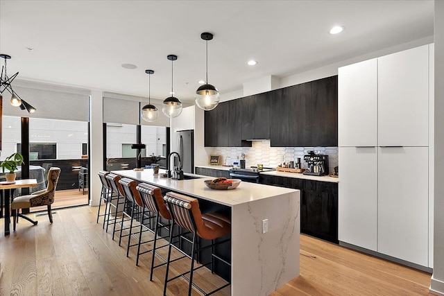 kitchen featuring sink, a kitchen island with sink, hanging light fixtures, stainless steel appliances, and decorative backsplash