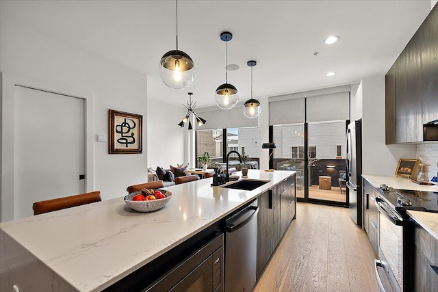 kitchen with sink, light hardwood / wood-style flooring, appliances with stainless steel finishes, a kitchen island with sink, and hanging light fixtures