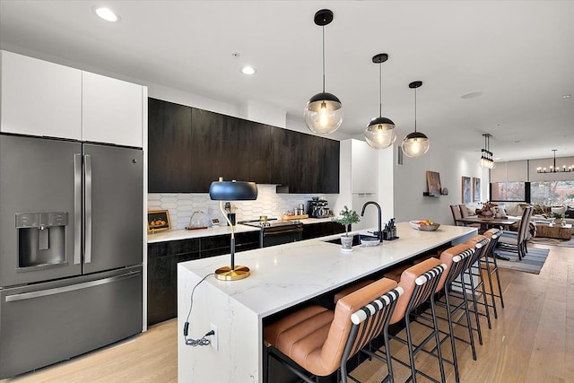 kitchen featuring stainless steel fridge with ice dispenser, decorative light fixtures, sink, and a center island with sink