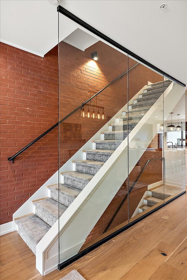 stairs with brick wall and hardwood / wood-style floors