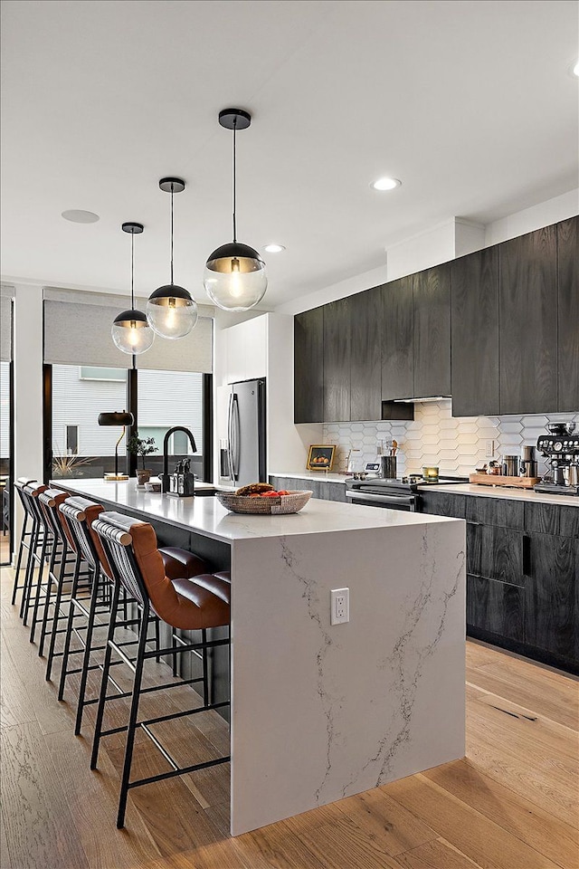 kitchen with appliances with stainless steel finishes, a kitchen breakfast bar, hanging light fixtures, a kitchen island with sink, and light hardwood / wood-style flooring