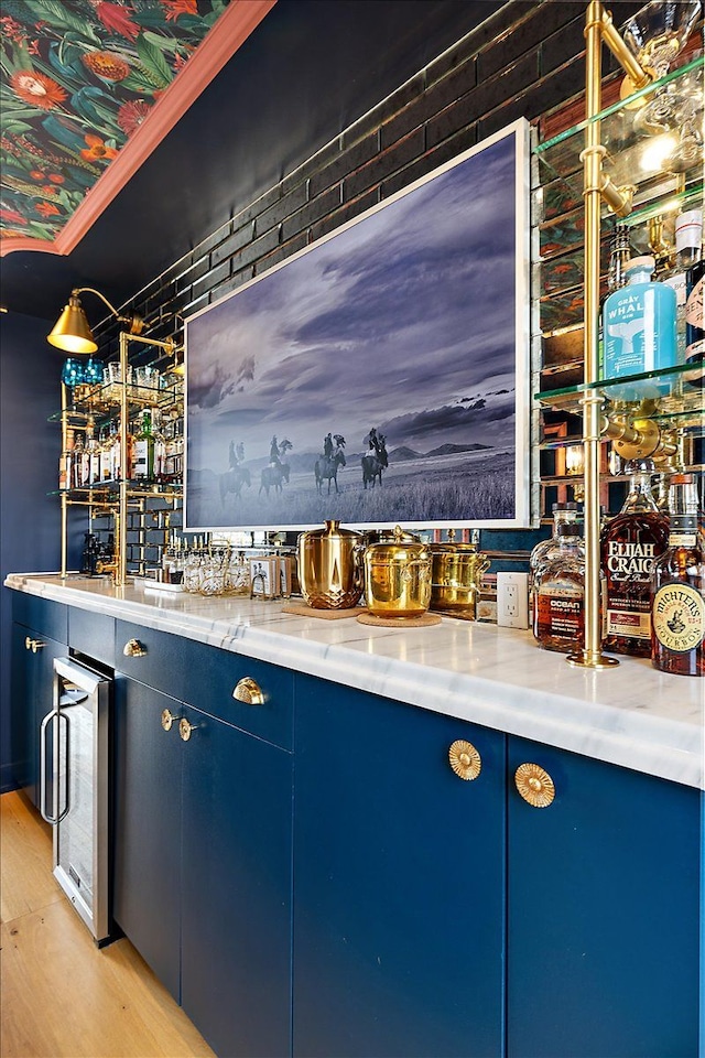 bar with blue cabinets, wine cooler, and light hardwood / wood-style floors