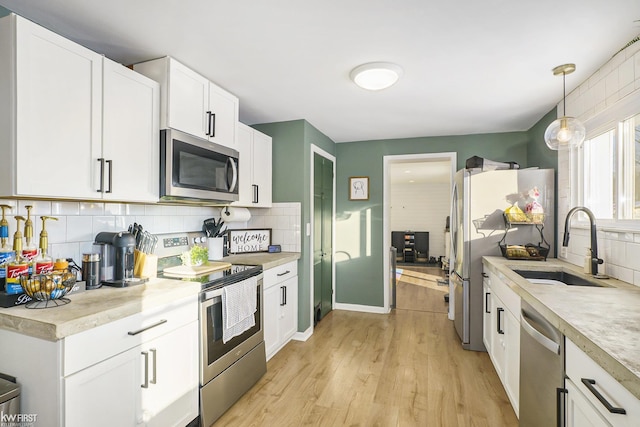 kitchen featuring sink, pendant lighting, stainless steel appliances, decorative backsplash, and white cabinets