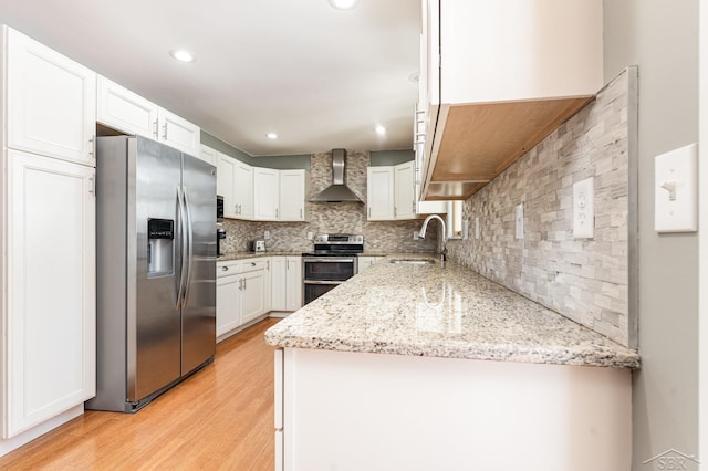 kitchen featuring wall chimney range hood, sink, white cabinetry, stainless steel appliances, and light stone counters