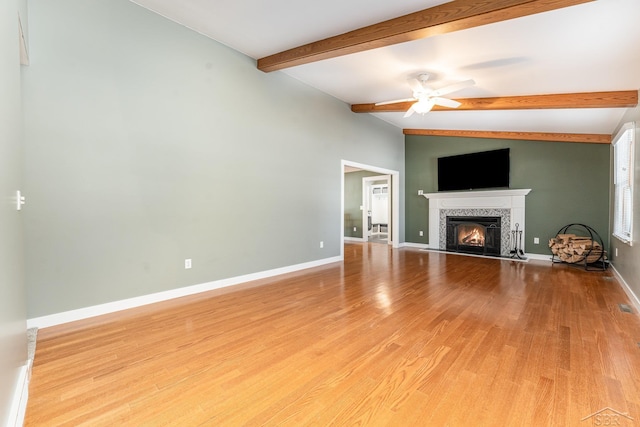 unfurnished living room with ceiling fan, light hardwood / wood-style floors, lofted ceiling with beams, and a tile fireplace