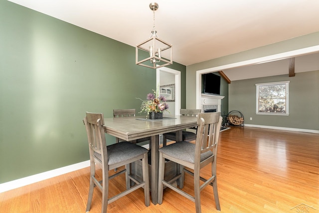 dining space featuring vaulted ceiling with beams, a chandelier, and light hardwood / wood-style floors