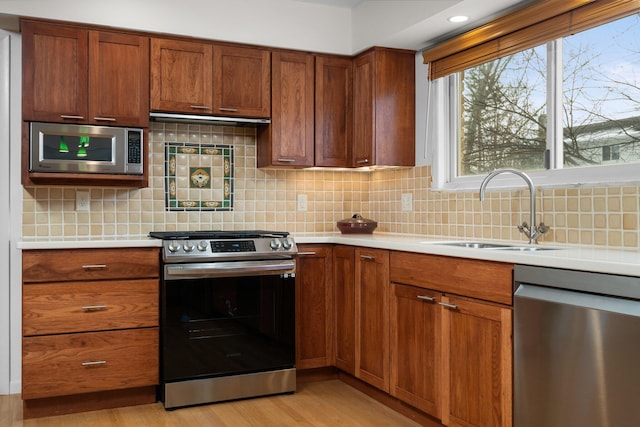 kitchen with appliances with stainless steel finishes, light hardwood / wood-style floors, sink, and backsplash