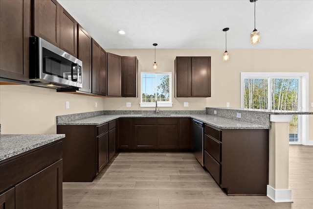 kitchen with pendant lighting, appliances with stainless steel finishes, light stone counters, light hardwood / wood-style floors, and kitchen peninsula