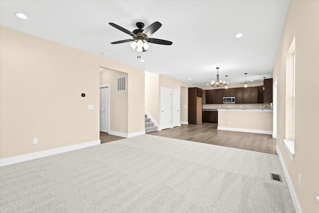 unfurnished living room featuring carpet flooring and ceiling fan with notable chandelier