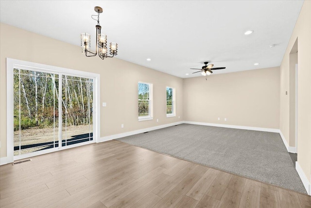 empty room with ceiling fan with notable chandelier and light hardwood / wood-style floors