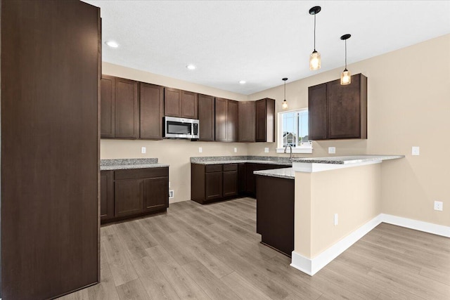 kitchen featuring sink, hanging light fixtures, dark brown cabinetry, light hardwood / wood-style floors, and kitchen peninsula