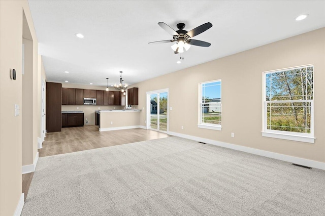 unfurnished living room featuring ceiling fan with notable chandelier and light hardwood / wood-style floors